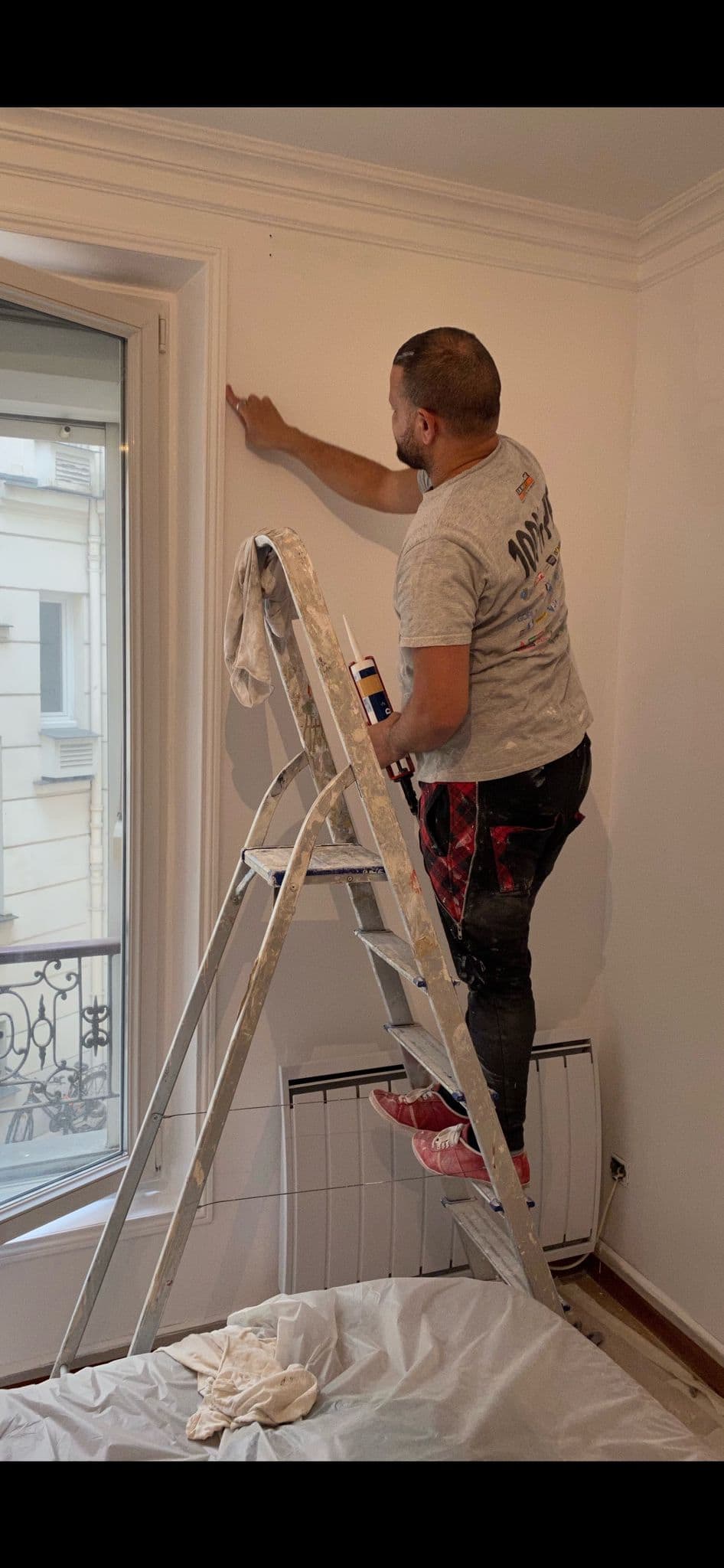 Peintre appliquant la finition en haut d’un mur, sol et menuiseries protégés